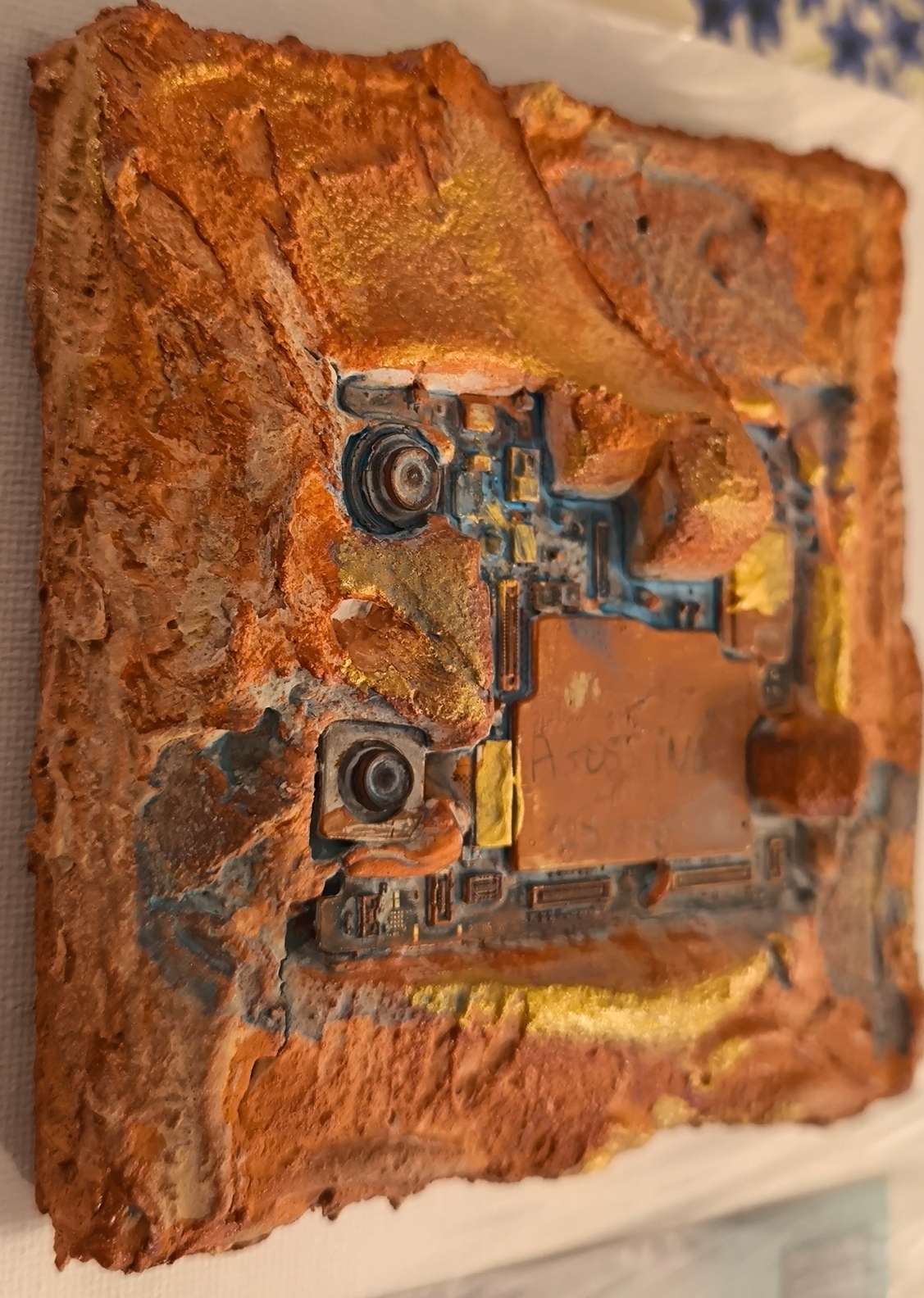 Détails en vue latérale de process cybernétique de téléphone intégré dans des matières de sables et pigments ocrés de Provence. Les textures sont rehausées d'or. Tableau contemporain unique en relief de François Tapiézo.