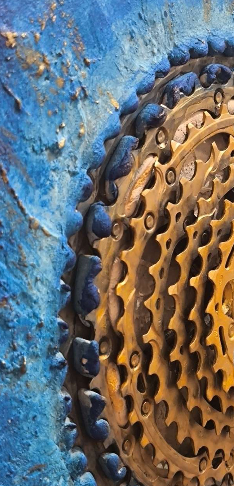 Détail en vue latérale d'une cassette de vélo, pièce industrielle qui devient un soleil doré. Textures sables et pigments de Roussillon en Provence, rehaussés à l'or, œuvre unique contemporaine, solaire et originale de François Tapiézo